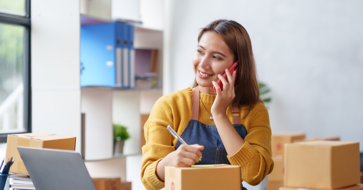 Mujer atendiendo una llamada de un cliente mientras anota detalles, en su negocio